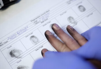 Police officer in exam gloves taking fingerprints from suspect, hands closeup