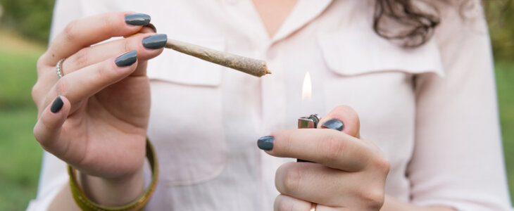 The young person smoking medical marijuana joint outdoors. The young woman smoke cannabis blunt, close-up. Cannabis is a concept of herbal alternative medicine.