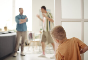 Rear view of little boy looking out from behind door and watching for quarrel of adults