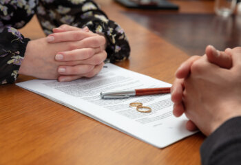 Signing a divorce, marriage dissolution documents and agreement. Wife and husband hands, wedding rings and legal papers for signature on a wooden table, lawyer office