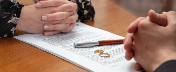 Signing a divorce, marriage dissolution documents and agreement. Wife and husband hands, wedding rings and legal papers for signature on a wooden table, lawyer office